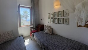 Un dormitorio con dos camas, una ventana con vistas, una lámpara de pared y cuadros enmarcados.