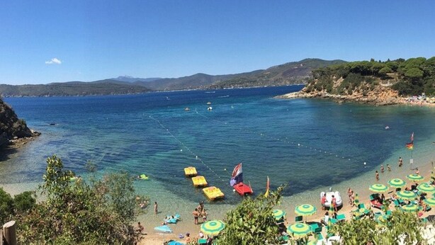 Una playa con agua cristalina, sombrillas y gente.
