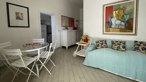 Un comedor con una mesa redonda y sillas, un sofá con cojines estampados y un cuadro en la pared.