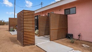 A building with corrugated metal gates, a concrete pathway, and a pink exterior wall. - Joshua Tree Oasis • Cowboy Pool • Hot Tub • 5 Private Acres (Yucca Valley)