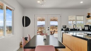 A modern kitchen with a black countertop, wooden cabinets, and a view of the desert through the sliding doors. - Joshua Tree Oasis • Cowboy Pool • Hot Tub • 5 Private Acres (Yucca Valley)