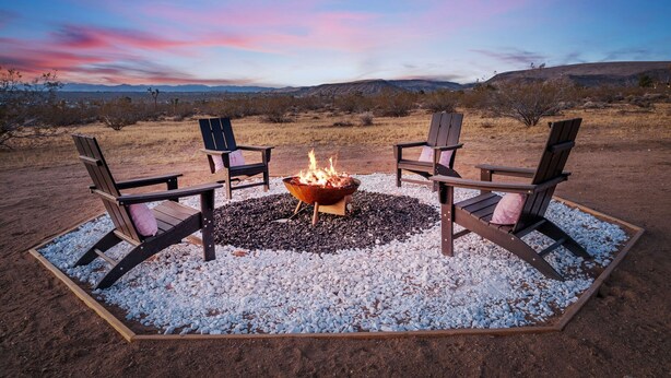 A fire pit with four Adirondack chairs arranged around it in a desert setting. - Joshua Tree Oasis • Cowboy Pool • Hot Tub • 5 Private Acres (Yucca Valley)