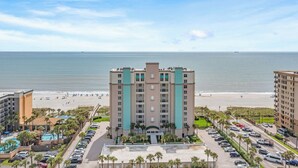 A hotel with a pool, beach view, and parking lot.
