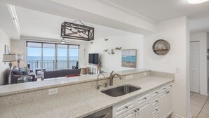 A kitchen with a large island, a built-in sink, and a view of the ocean through a large window.
