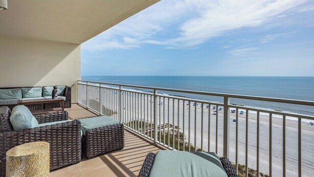 A balcony with wicker furniture, a view of the beach, and a railing.