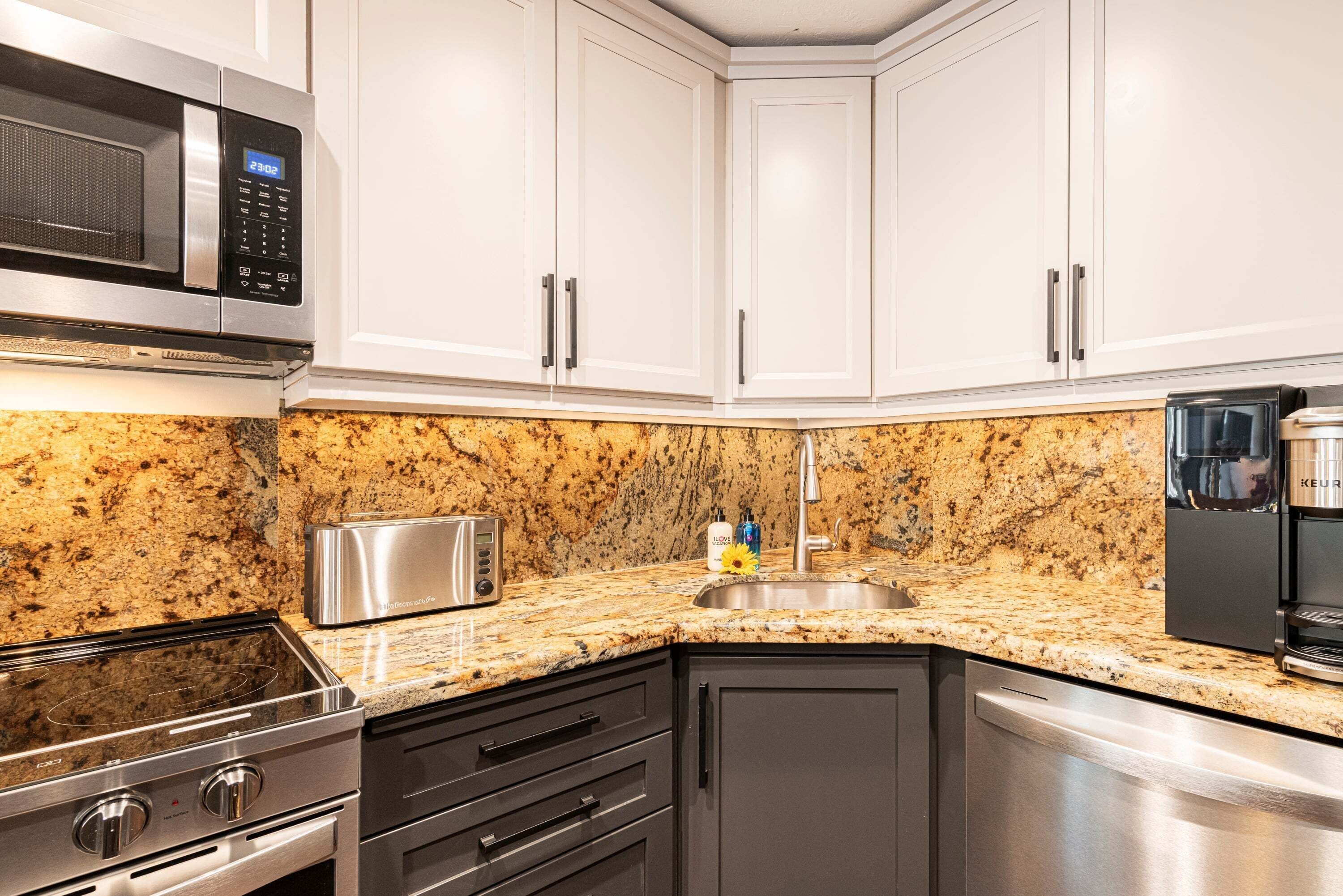 A kitchen with white cabinets, a granite countertop, a microwave, a toaster, a sink, and a dishwasher.
