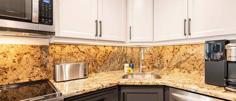 A kitchen with white cabinets, a granite countertop, a microwave, a toaster, a sink, and a dishwasher.