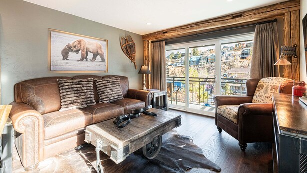A living room with a brown leather sofa, a wooden coffee table, a large window with a view of buildings, and a mounted bear picture on the wall. - Rustic Luxe on Main | Spa, Dining & Charm On-Site at the Treasure Mountain Inn (Park City)