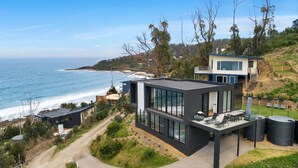 Une maison moderne dotée de grandes baies vitrées, d’un balcon et offrant une vue sur l’océan.