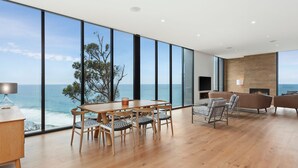 Une pièce spacieuse dotée d’une grande fenêtre donnant sur la mer, d’une table à manger en bois avec des chaises, d’une cheminée et d’un coin salon avec des canapés.