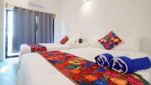 Een hotelkamer met twee bedden, een kleurrijk bloemenbedekking, wit beddengoed en een raam met gordijnen.