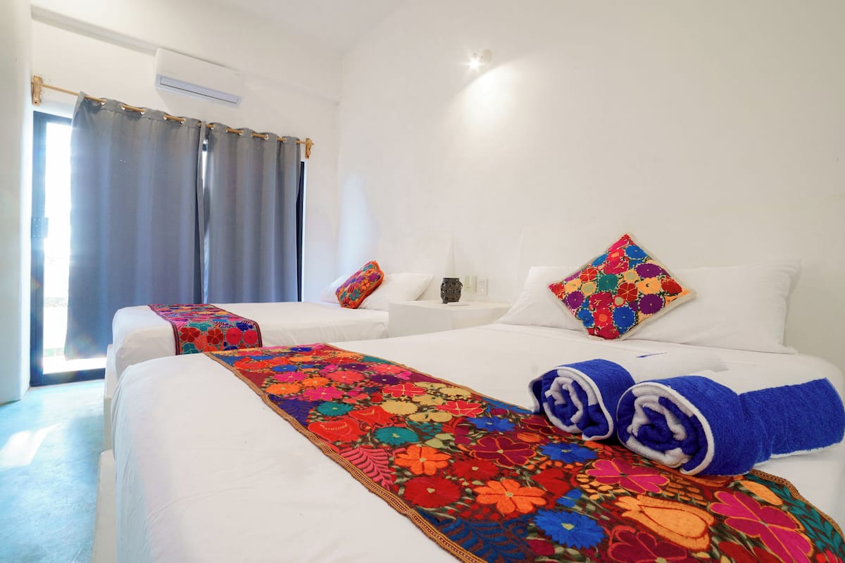 A hotel room with two beds, a colorful floral bedspread, white bedding, and a window with curtains.