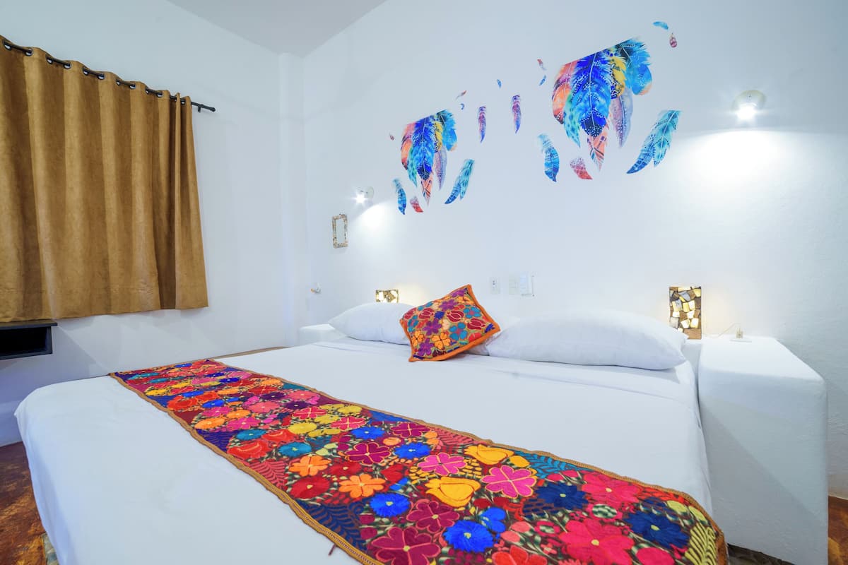 A hotel room with a bed, a colorful floral bedspread, a brown curtain, and wall art.