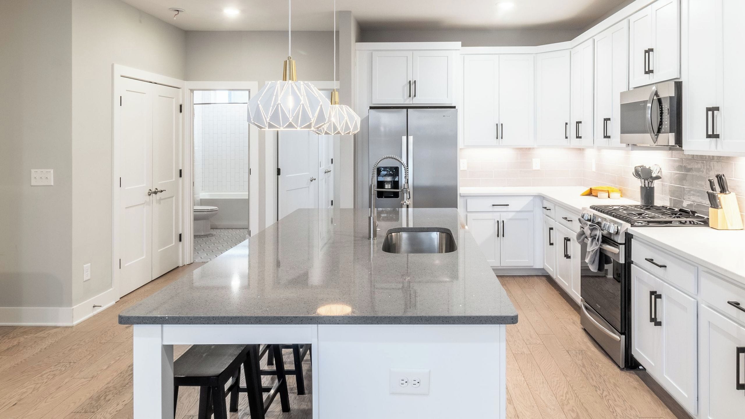A modern kitchen with white cabinetry, a central island, stainless steel appliances, and a pendant light.