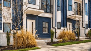 Fileira de casas urbanas com fachada de tijolo, janelas amplas e pequeno jardim frontal com plantas.