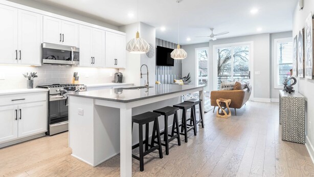 A modern kitchen with white cabinetry, a central island with bar stools, a built-in microwave, and a stove. - Monty by Avantstay 4bdr 4ba, Balcony w/ Outdoor Seating, 5mins to DT (Nashville)
