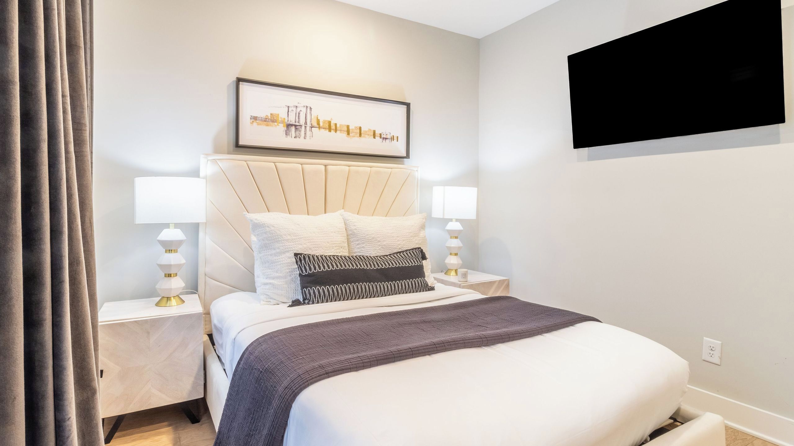 A neatly arranged bedroom with a bed, two bedside tables, a wall-mounted TV, and a framed picture above the bed.