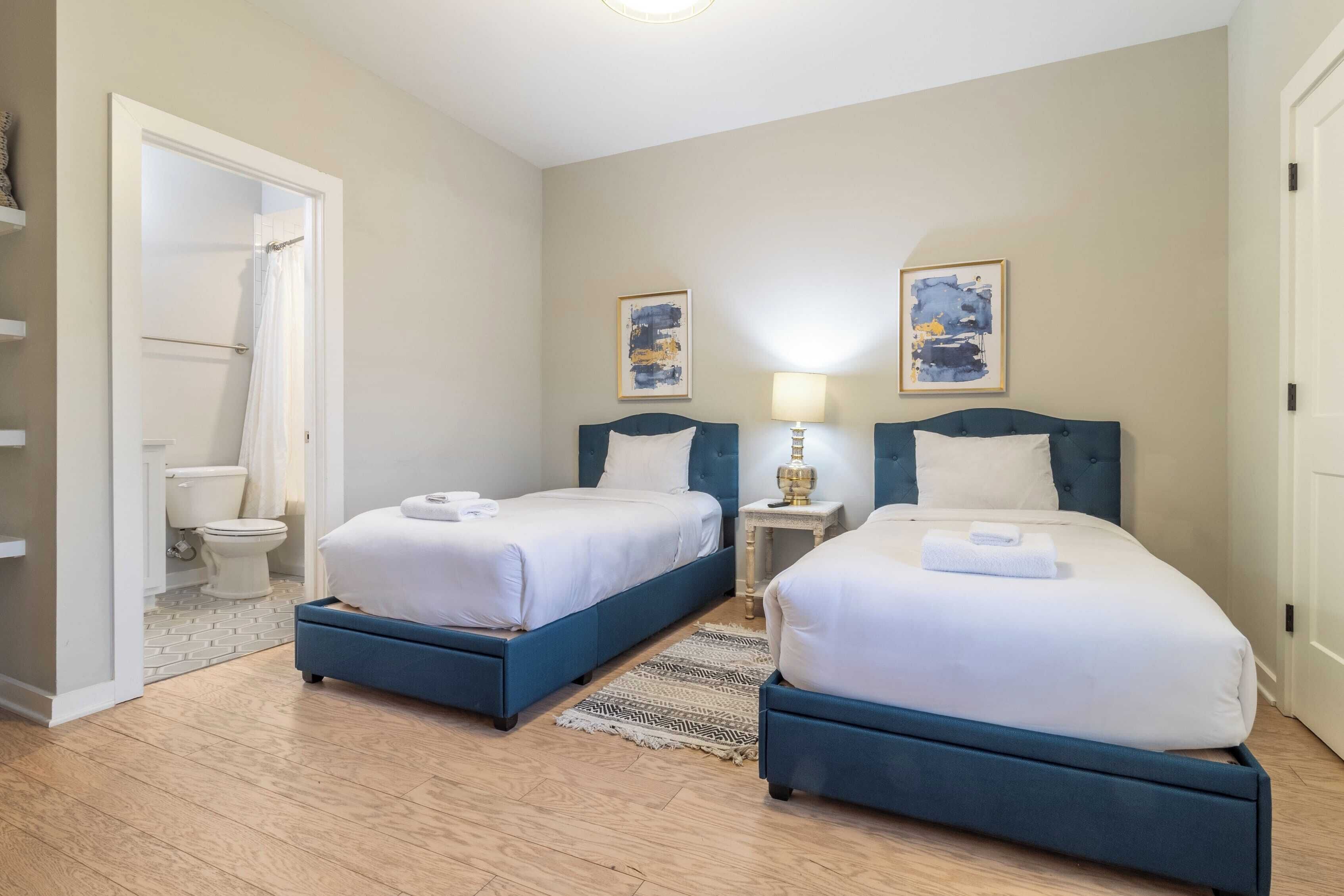 A hotel room with two beds, a bathroom, and a small bedside table with a lamp.