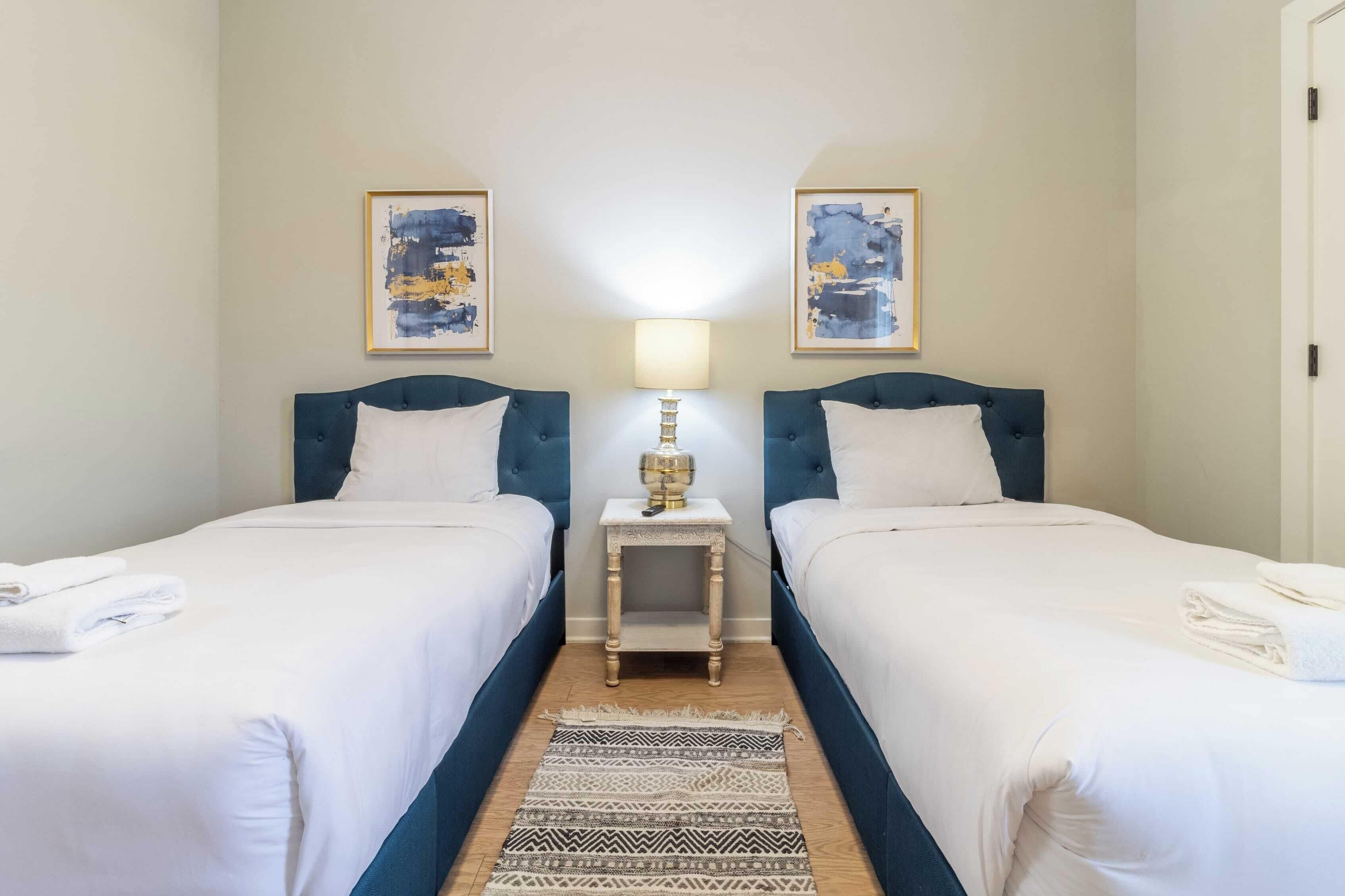A hotel room with two beds, a nightstand with a lamp, and artwork on the walls.