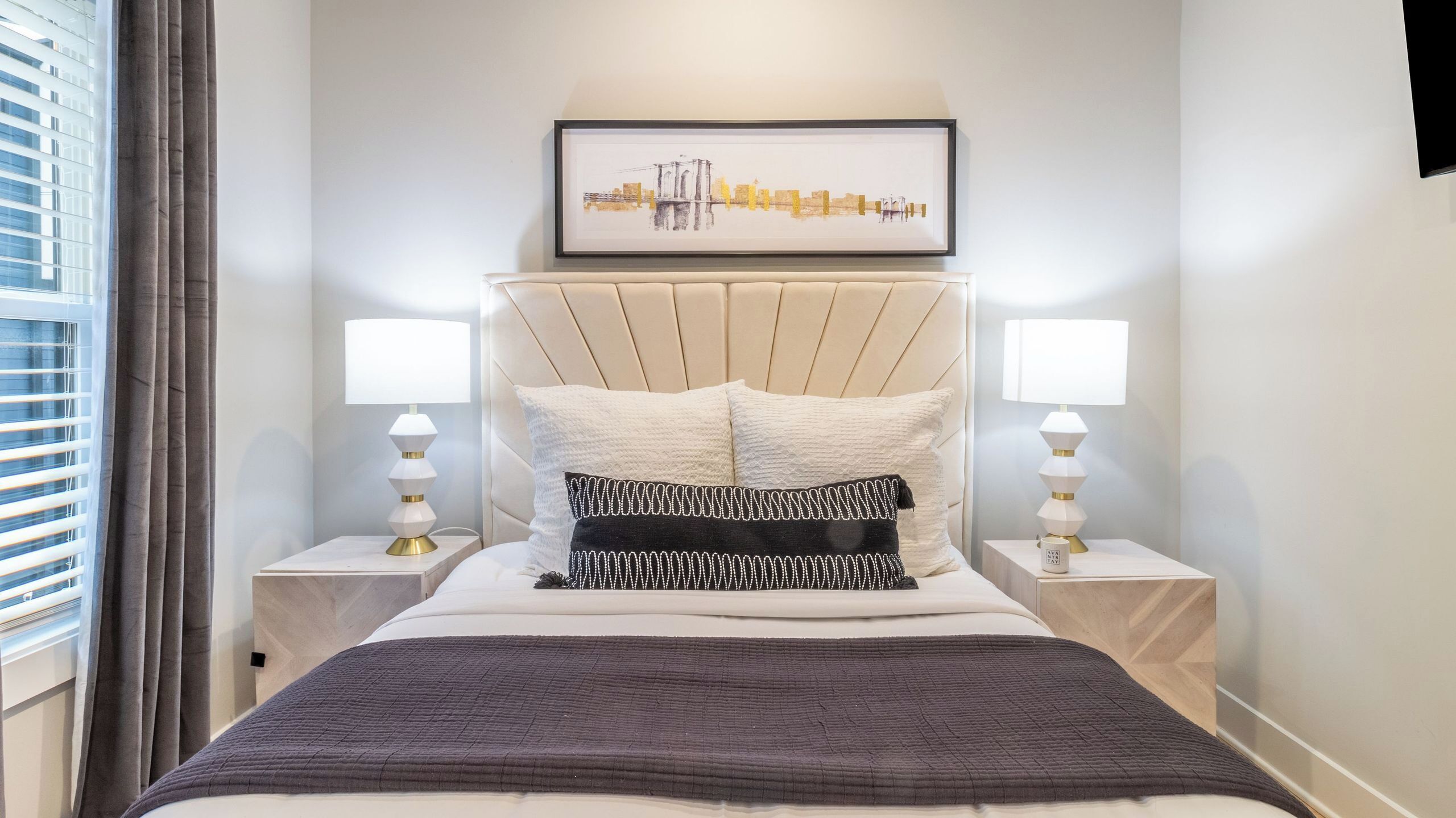 A neatly arranged bedroom with a bed, two bedside tables, a headboard, and a framed artwork above the bed.