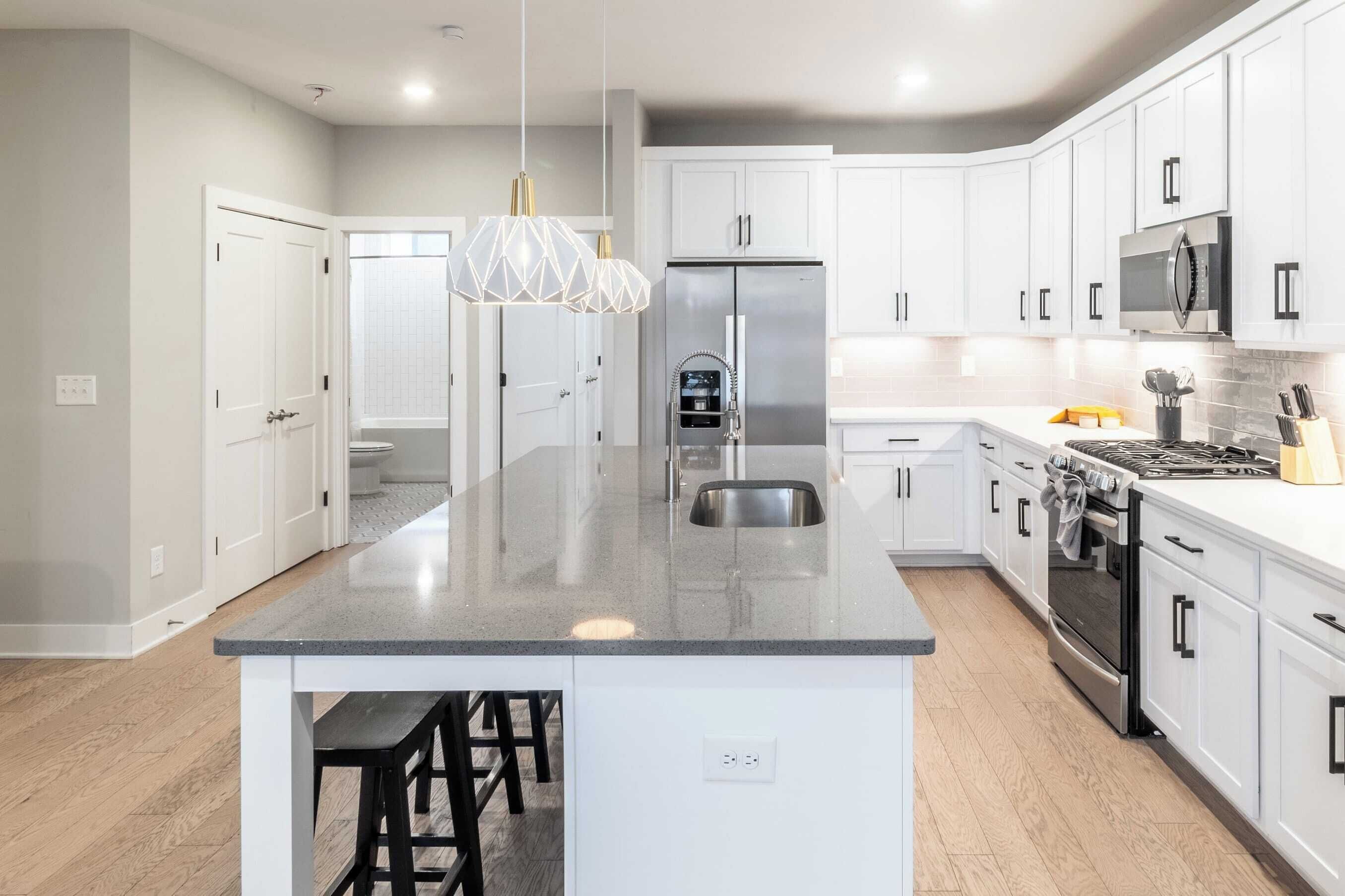 Una cocina moderna con armarios blancos, electrodomésticos de acero inoxidable y una isla central con taburetes de bar.