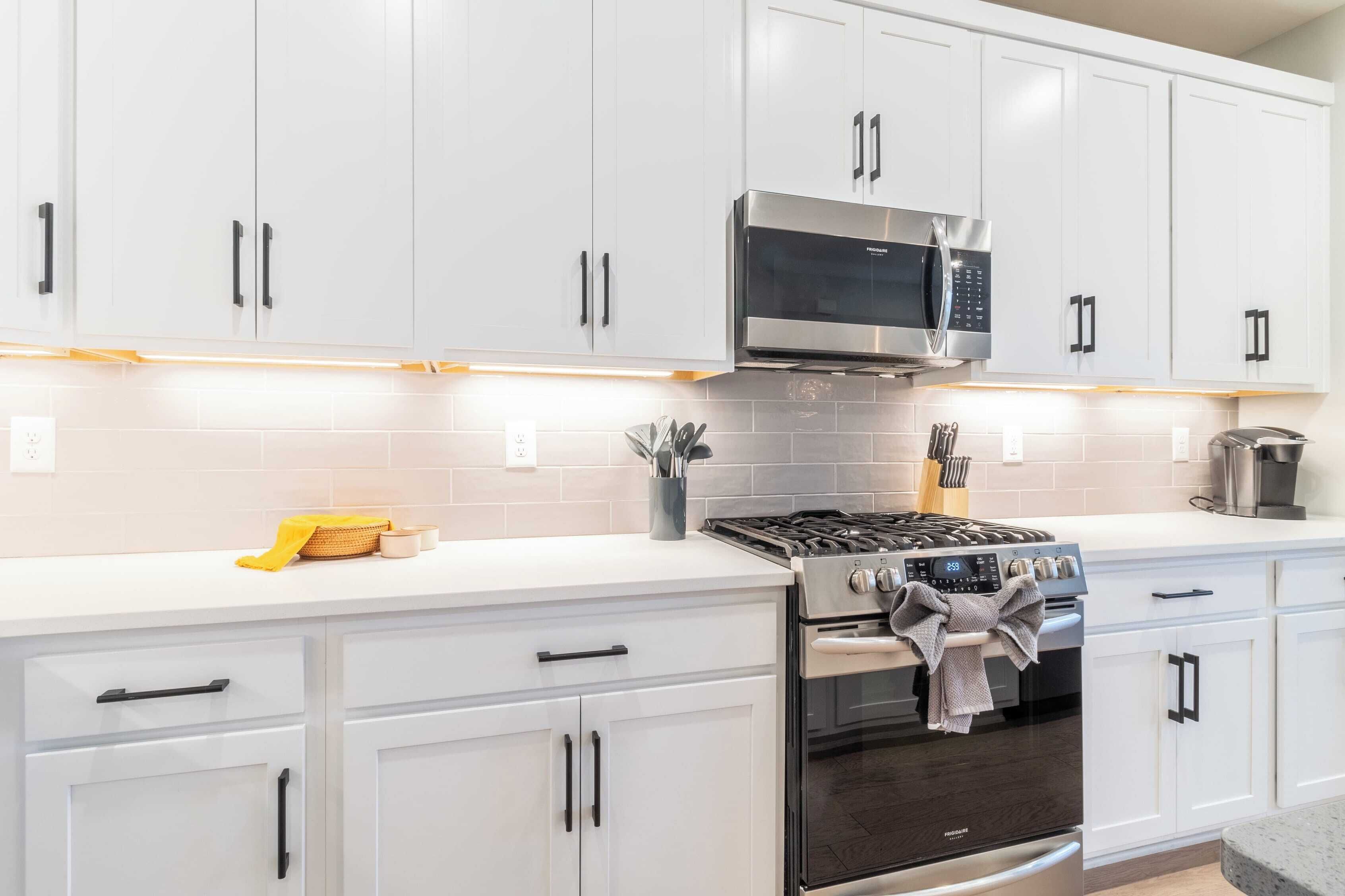 A modern kitchen with white cabinets, a stainless steel microwave, a gas stove, and a built-in oven.