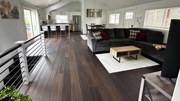 A spacious living area with a dark wood floor, a grey sofa with patterned cushions, a wooden coffee table, and a dining area with a table and chairs. - Redlands farm (Oregon City)