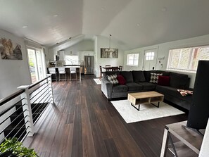 A spacious living area with a dark wood floor, a grey sofa with patterned cushions, a wooden coffee table, and a dining area with a table and chairs. - Redlands farm (Oregon City)