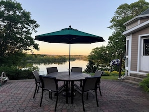 A patio with a table and chairs, an umbrella, and a view of a lake.