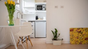 Een moderne keuken met witte kasten, een magnetron en een spoelbak. Er is een eethoek met een witte tafel en stoelen, en een potplant.