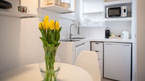 Een moderne keuken met witte kasten, een magnetron en een spoelbak. Op een tafel staat een vaas met gele tulpen.