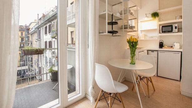 Een moderne keuken met witte kasten, een magnetron en een eethoek met een witte tafel en stoelen.
