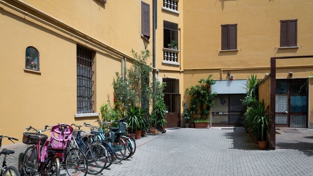 Een binnenplaats met fietsen langs de muur, planten in potten, en een gebouw met balkons en ramen.