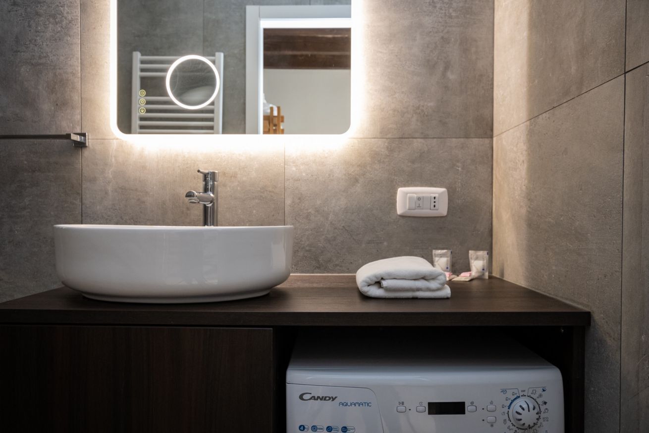 A bathroom with a large white sink, a mirror, a towel, and a Candy Aquamatic washing machine.