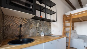 Cocina compacta con encimera de madera, pileta negra y una estantería empotrada.