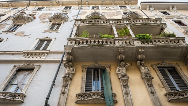 Fachada de edificio con balcones ornamentados, molduras decorativas y una serie de ventanas.