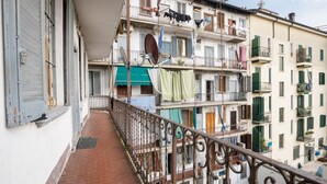 Un balcón estrecho con barandilla de hierro forjado, con vistas a un edificio de varios pisos con balcones y ventanas.