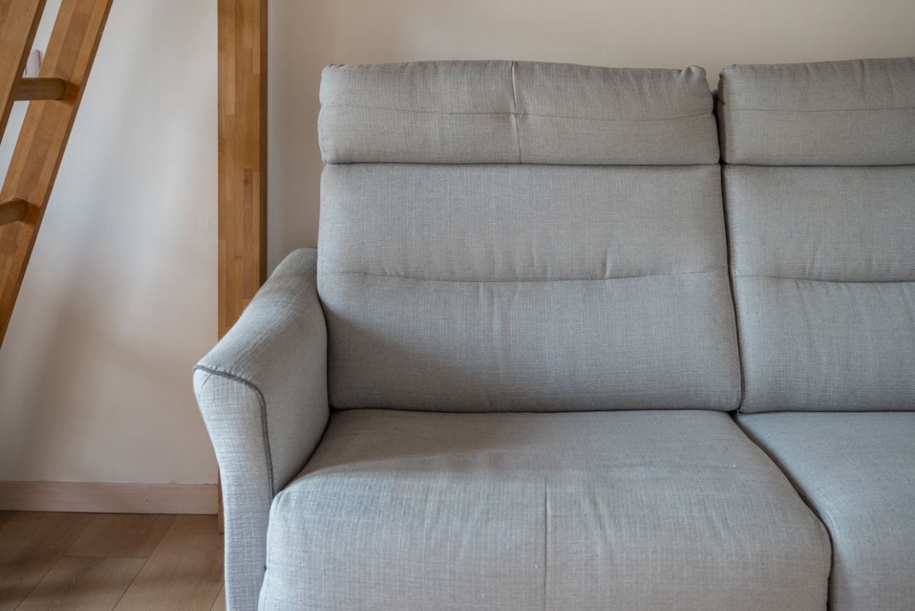 A grey sofa with a wooden slat wall behind it.