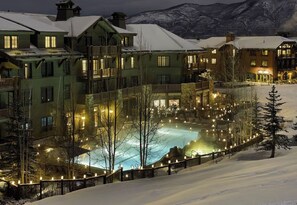 Ein schneebedecktes Resort mit einem zentralen Pool, mehreren Gebäuden und einer Bergkulisse.