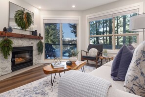 Una sala de estar acogedora con chimenea, un ventanal con vistas a un bosque, un sofá cómodo y una mesa de centro de madera.
