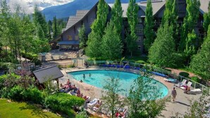 A resort with a large pool surrounded by lounge chairs and a mountainous backdrop.