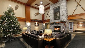 A cozy lobby with a Christmas tree, leather sofas, a stone fireplace, and ski equipment on the wall.