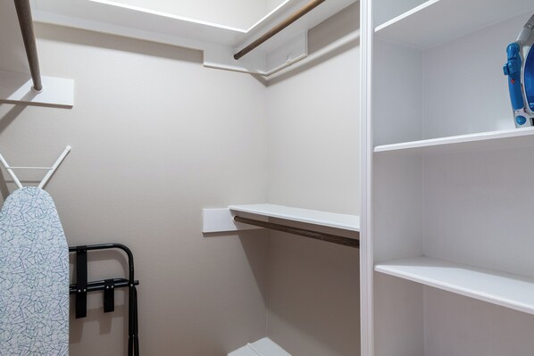A corner of a room with white walls, a black metal rack with an ironing board, and a blue item on a shelf.