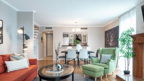 Ein modernes Wohnzimmer mit einer Couch, einem Sessel und einem Couchtisch. Im Hintergrund befindet sich ein Essbereich mit Stühlen und einem Tisch.