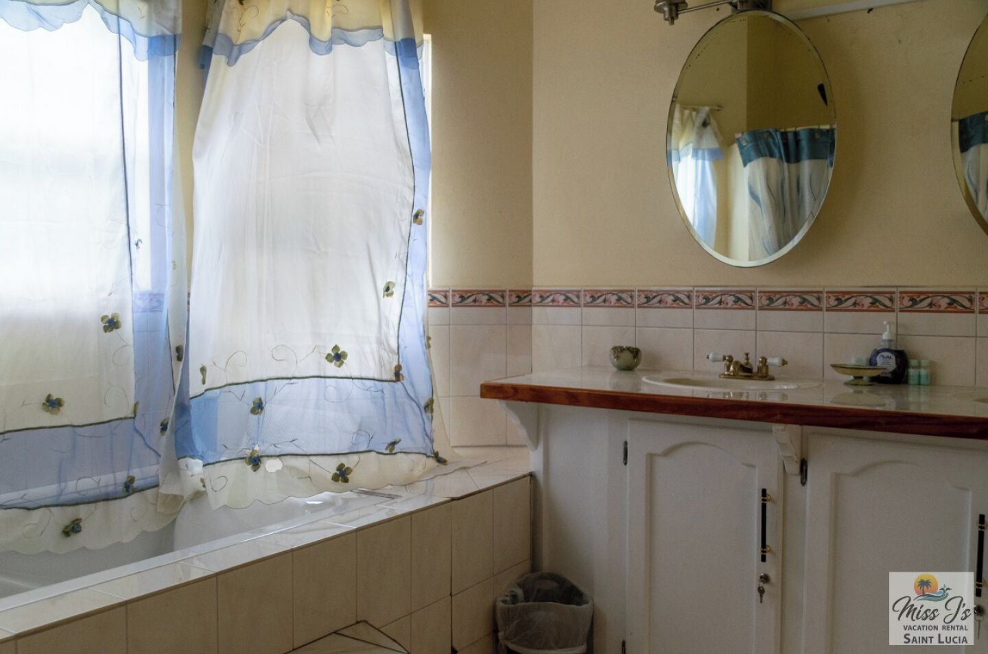 Un baño con bañera, lavabo, espejo y ventana con cortina estampada.