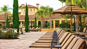 A poolside area with lounge chairs and umbrellas, a fountain, and a building with a tiled roof. - VIP access to WorldQuest Resort with no extra fees (Orlando)