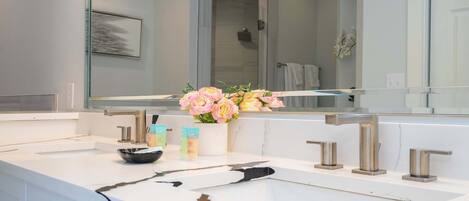 Ein Badezimmer mit einem weißen Marmorwaschbecken, einem großen Spiegel und einer Vase mit Blumen.
