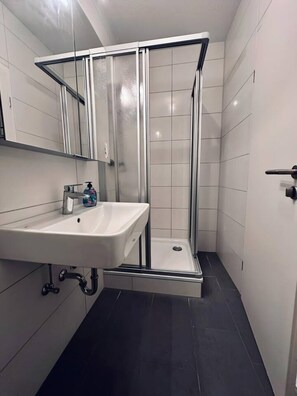 Ein Badezimmer mit Duschkabine, Waschbecken und Spiegel.