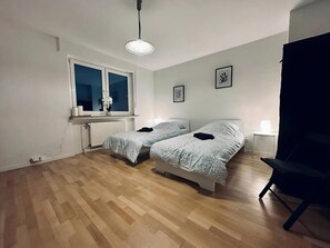 Ein Schlafzimmer mit zwei Betten, einem Heizkörper, einem Fenster und einem Sessel.