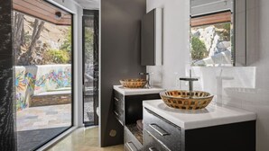 Een moderne badkamer met een groot raam, twee wasbakken met decoratieve kommen en een donkere kast.